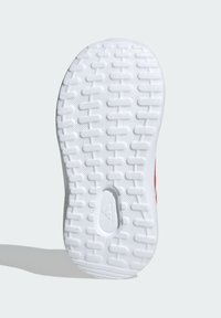 Biała podeszwa sneakerów o fakturowanej, rowkowanej powierzchni, z okrągłym wycięciem i subtelnym detalem brandowym. Czerwone akcenty w pobliżu boku.
