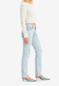 Ljust blå denimjeans med rak passform, kombinerat med en kort, fluffig vit tröja och ljusbl å spetsiga klackar.