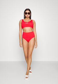 Conjunto de biquíni vermelho de duas peças com um top cropped ajustado e parte de baixo de cintura alta. Feito de um tecido suave com mínima marcação e detalhes. Sandálias brancas.