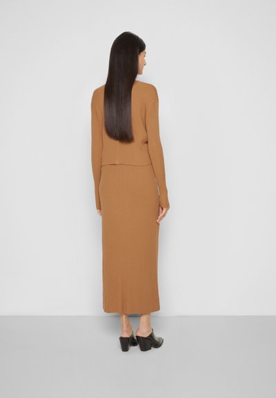 Top de manga longa castanho com riscas, combinado com uma saia maxi de riscas a condizer. Textura suave e design justo. Sapatos de salto bloco pretos.