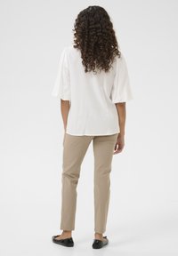 Blusa bianca con maniche a palloncino corte, abbinata a pantaloni slim-fit beige chiaro e ballerine nere, vista da dietro su uno sfondo neutro.