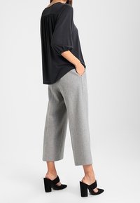 Černá, volně padnoucí blůza s plisovaným zadním dílem; šedé široké kalhoty; černé otevřené lodičky na blokovém podpatku.