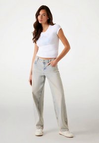 White short-sleeve crop top with a light graphic, paired with lightwash wide-leg jeans and white sneakers. Smooth, casual cotton fabric.