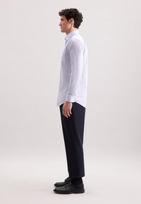 Jasnoniebieska koszula w kratkę z długim rękawem, zestawiona z ciemnogranatowymi spodniami i czarnymi butami, widziana z boku.