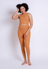 Conjunto de activewear de dos piezas en color beige ribeteado, que incluye un top corto con cuello alto y leggings de tiro alto, ambos en un tejido suave y elástico.