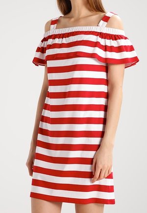 Femme portant une robe rouge et blanche à rayures horizontales, épaules dénudées, avec un col à volants et des fines bretelles.