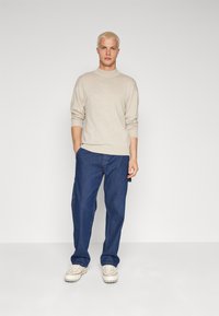 Suéter de punto beige, jeans azules holgados y zapatillas blancas. Ajuste casual con puños acanalados y cuello redondo. Color sólido, diseño minimalista.
