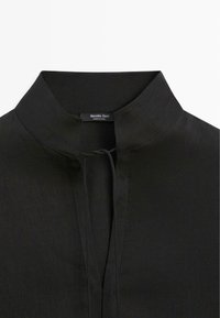 Schwarzes Hemd mit hohem Kragen, kleinem offenem Schlitz am Hals und sichtbarem Markenetikett "Massimo Dutti" innen.