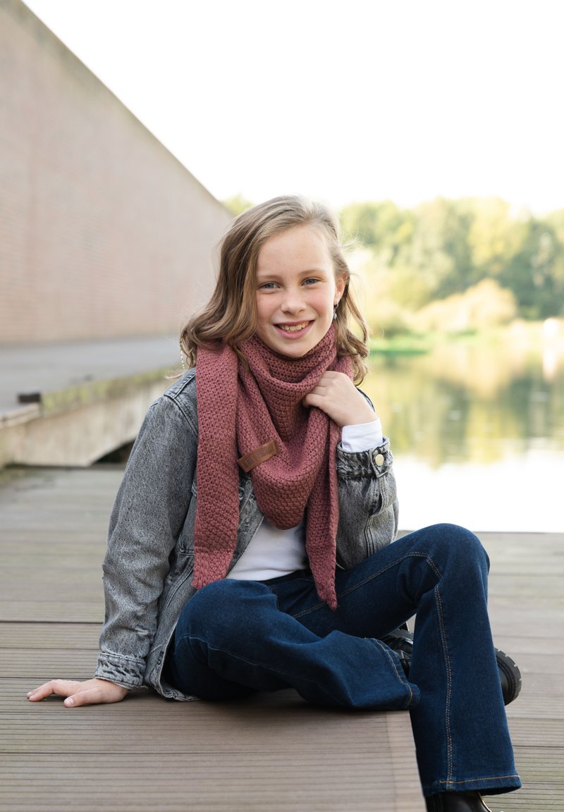 Gebreide bordeauxrode sjaal met een gestructureerd patroon en een bruin leren accent, gedragen over een witte top en een grijs denim jack, zittend op houten planken.