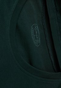 Ciemnozielona koszulka z okrągłym dekoltem, gładką teksturą i kontrastowym niebieskim szwem. Metka pokazuje rozmiar L i nazwę marki.