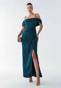 Cyan satijnen jurk met off-shoulder mouwen, een getailleerde bodice en een zijsplit. Gecombineerd met strappy sandalen en een kleine gouden clutch.