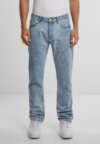 Lyseblå denimjeans med rett passform, fem lommer, metallknappe-lukking og subtil falming, kombinert med hvite joggesko.