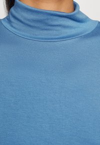Blå turtleneck-top i ett mjukt, lätt tyg. Har en hög krage och figursydd siluett, med en enfärgad design och inga synliga mönster.