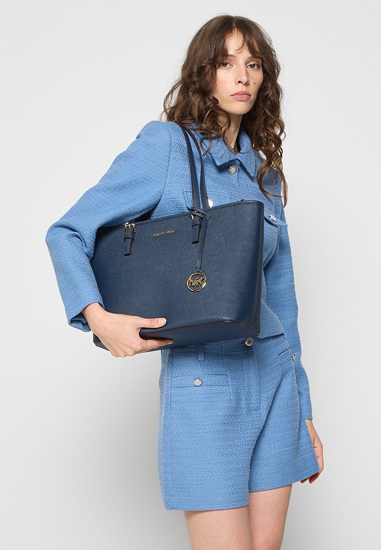 Sac cabas structuré bleu marine avec une finition texturée, des poignées doubles, des accents en matériel doré et un pendentif logo à l'avant.