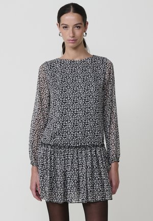 Vestido de estampado en blanco y negro con mangas largas, escote redondo y cintura fruncida. Hecho de una tela ligera y transparente con una falda plisada.