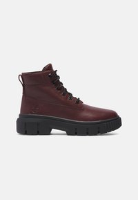 Bottine à lacets en cuir rouge foncé avec une semelle épaisse noire à crampons et une languette d'extraction à l'arrière.