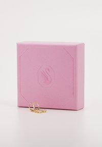 Ružová textúrovaná darčeková škatuľa s embosovaným logom, sprevádzaná tromi zlatými prsteňmi, dvoma s priesvitnými kameňmi a jedným hladkým štýlom.