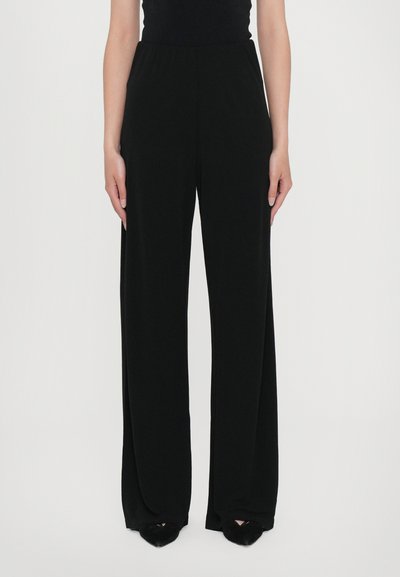 Pantaloni negri cu pantalon evazat, dintr-un material neted, cu talie și care ajung până la gleznă. Purtați cu pantofi negri cu vârf ascuțit.