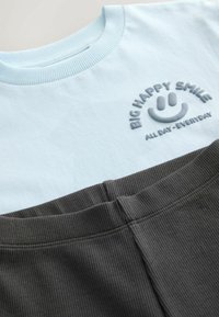 Světle modré bavlněné tričko s žebrovaným výstřihem a šedým vyšitým textem; spárované s tmavě šedými žebrovanými šortkami s elastickým pasem.