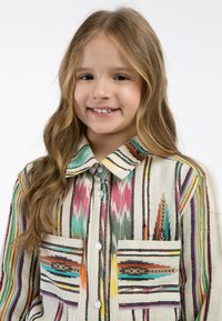 Camicia a strisce verticali multicolore con un colletto e due tasche frontali con design intricati. Realizzata in tessuto intrecciato.