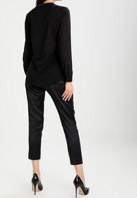 Femme de dos portant un haut noir à manches longues, un pantalon noir court avec des rayures sur les côtés et des chaussures à talons hauts noires.