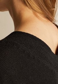 Schwarzes Strickkleidungsstück mit strukturiertem Oberflächen. Verfügt über einen weit ausgeschnittenen Halsausschnitt und sichtbare Nähte entlang der Schulternaht. Keine Muster oder Beschläge.