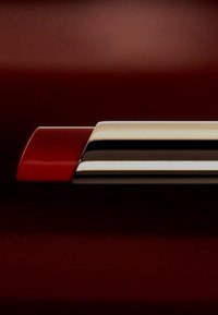 Lippenstift mit einer glänzenden roten Hülse und silbernem Metallgehäuse, das ein schlankes Design mit glatter Textur und geschwungener Form aufweist.