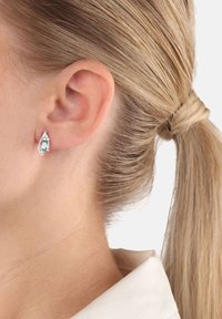 Droppformade silverörhängen med en central smaragdsten, omgiven av små klara accenter, visade sig mot ljust hår och hud.