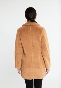 Tan faux fur frakke med krave, lange ærmer og en afslappet pasform. Blødt, tekstureret materiale. Lige bagsøm og knælangt design.