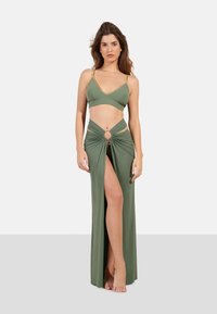 Bikini verde oliva con detalles dorados, combinado con una falda de envoltura a juego que presenta una abertura frontal y un detalle de corte circular.