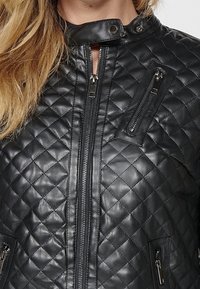 Giacca nera in pelle trapuntata con colletto alto, chiusura frontale a zip e due tasche laterali con zip e dettagli metallici.