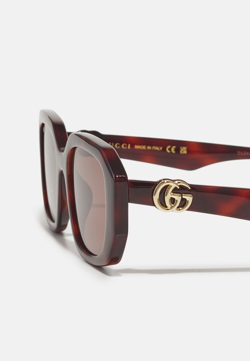 Lunettes de soleil Gucci avec des montures en plastique écaille de tortue foncé, de forme rectangulaire surdimensionnée, verres bruns et détails en or avec le logo GG sur la branche.
