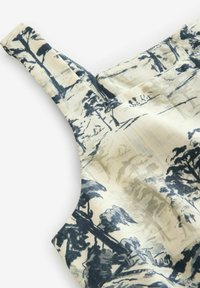 Débardeur en tissu beige avec imprimé paysage bleu foncé, comportant des bretelles larges et une texture lisse.