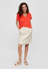 Rode V-hals t-shirt, beige linnen rok met elastische taille en zijzak, en beige sandalen met dikke zolen en geweven details.
