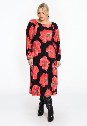 Schwarzes Kleid mit großem rotem Blumenmuster, langen Ärmeln und entspannter Passform. Tragen mit schwarzen kniehohen Stiefeln mit glatter Textur.