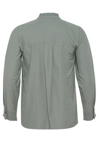 Long-sleeve shirt in light green fabric. Features ruffled collar and cuffs, buttoned sleeves, and a pleated back design. Smooth texture.