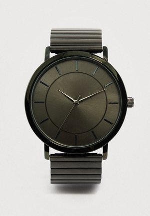 Sort metallur med et minimalistisk rundt urskive, børstet tekstur og tynde timemarkører. Har en ribbet sort rem og sølvfarvede visere.