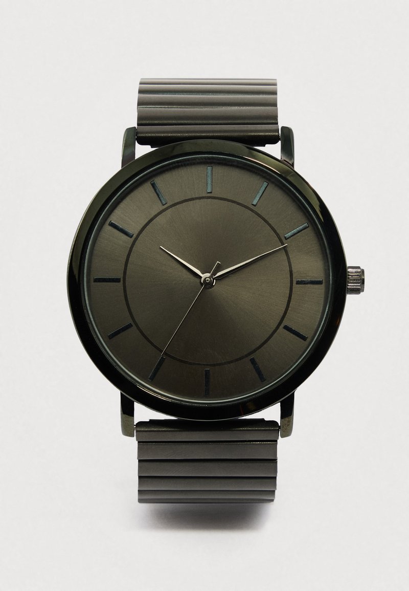 Μαύρο μεταλλικό ρολόι με μινιμαλιστικό στρογγυλό καντράν, βουρτσισμένη υφή και λεπτούς δείκτες ώρας. Διαθέτει ραβδώσεις στο μαύρο λουράκι και ασημένια δείκτες.