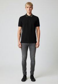 Černé polo tričko s vzorovaným límečkem, doplněné úzkými šedými džíny a černými teniskami. Čistý design a přiléhavý střih.