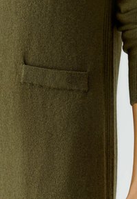 Olivgrüner Strickpullover mit strukturiertem Finish, ausgestattet mit einer einzelnen aufgesetzten Tasche und gerippten Akzenten an den Ärmeln und dem Saum.