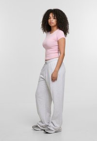 Hellrosa, enganliegendes T-Shirt, kombiniert mit lockeren grauen Jogginghosen und grauen Turnschuhen, die eine weiche Textur und einen elastischen Bund aufweisen.