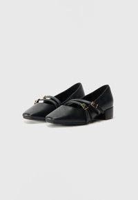 Décolleté in pelle nera con punta affusolata, tacco basso a blocco e cinturini decorativi incrociati con fibbie dorate. Texture liscia, design minimalista.