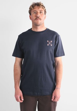 T-shirt en coton navy avec un petit motif floral coloré sur le côté gauche de la poitrine. Manches courtes et style col rond classique.