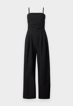 Μαύρη ολόσωμη φόρμα χωρίς μανίκια με λεπτές τιράντες, εφαρμοστό μπούστο και παντελόνι με φαρδιά πόδια σε απλό ανοιχτό φόντο.