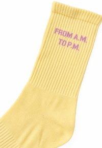 Chaussette côtelée jaune avec texte violet ""FROM A.M. TO P.M."" près du bord sur fond blanc.