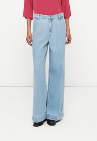 Lyseblå vide jeans laget av denim, med høy livvidde, knappelukking og oppbrettede kanter, kombinert med svarte hælsko.