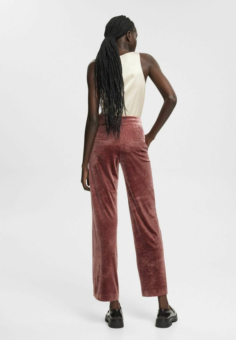 Rosa Samtweite-Hosen mit strukturiertem Finish, hoher Taille und Gesäßtaschen, kombiniert mit einem ärmellosen hellen Oberteil.