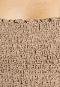 Tissu smocké beige texturé avec des fronces horizontales et un bord froncé en haut, couvrant la peau nue au-dessus.