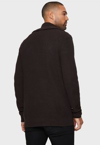 Brauner Strickcardigan mit weitem Kragen, langen Ärmeln und gerippter Textur. Mit einem lässigen Schnitt und subtilen Nahtdetails auf der Rückseite gestaltet.
