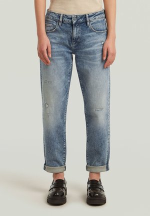 Lichtblauwe denim jeans met een relaxed fit, voorzien van distressed details, opgerolde boorden en klassieke vijf-pocket styling. Zwarte loafers eronder gedragen.